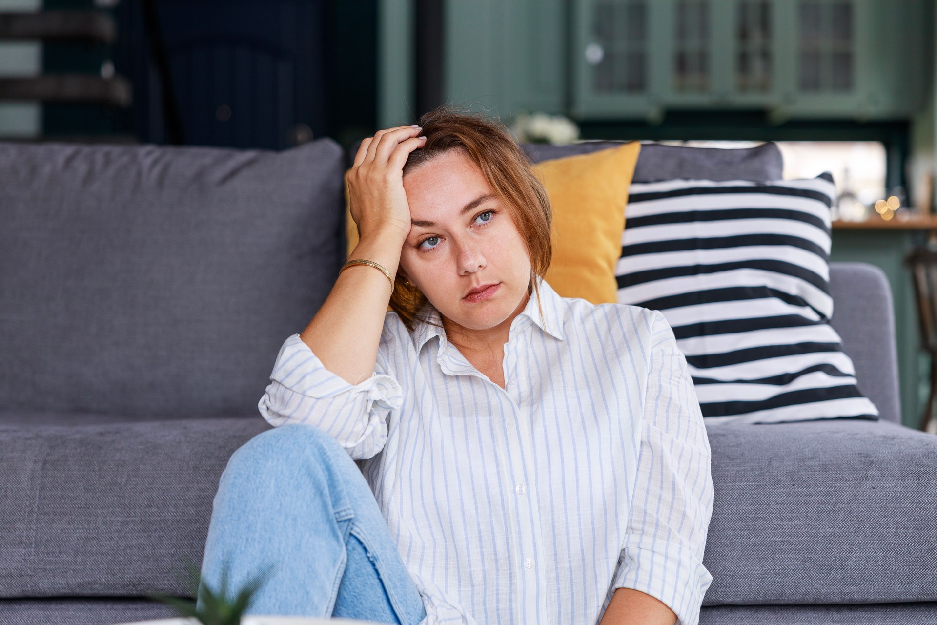 Depressed young woman sitting on living room floor at home