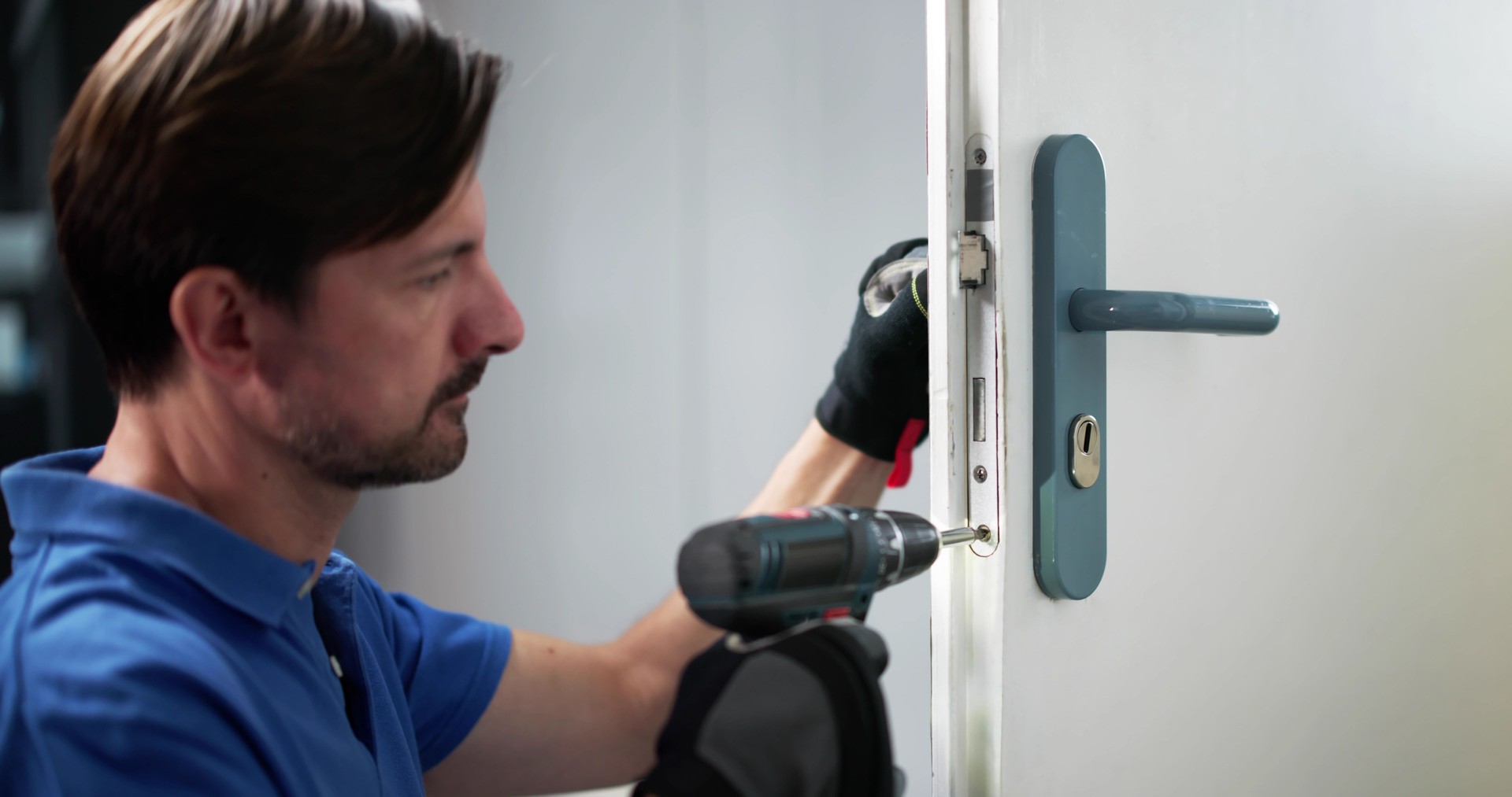Skilled Locksmith Carefully Installing New Lock On Customer's Front Door Skilled Locksmith Carefully Installing New Lock On Customer's Front Door